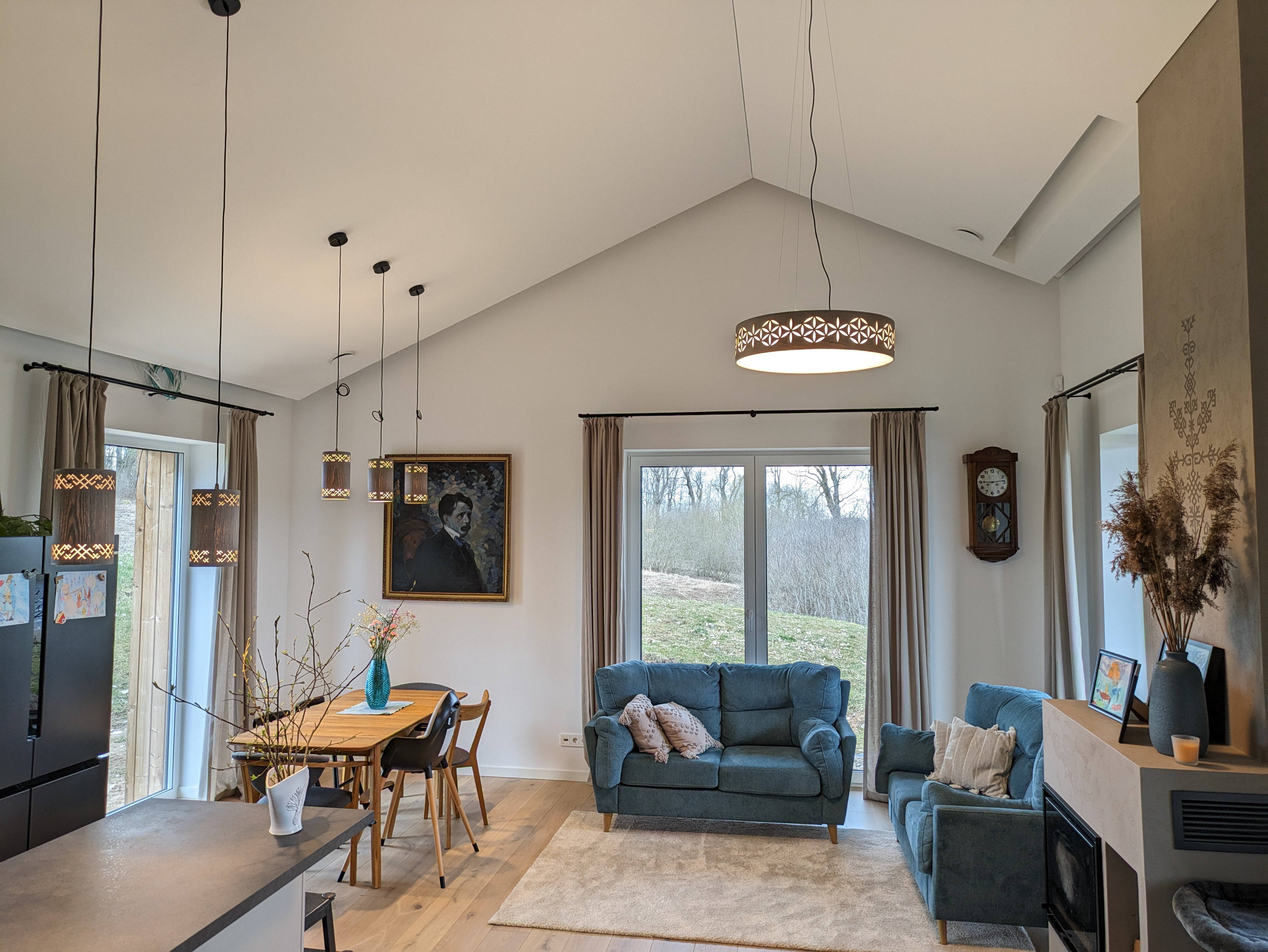 Lubinis šviestuvas nuleistas nuo šlaitinių lubų šviesiame interjere su pilko ąžuolo pakabinamais šviestuvais Žirgeliai